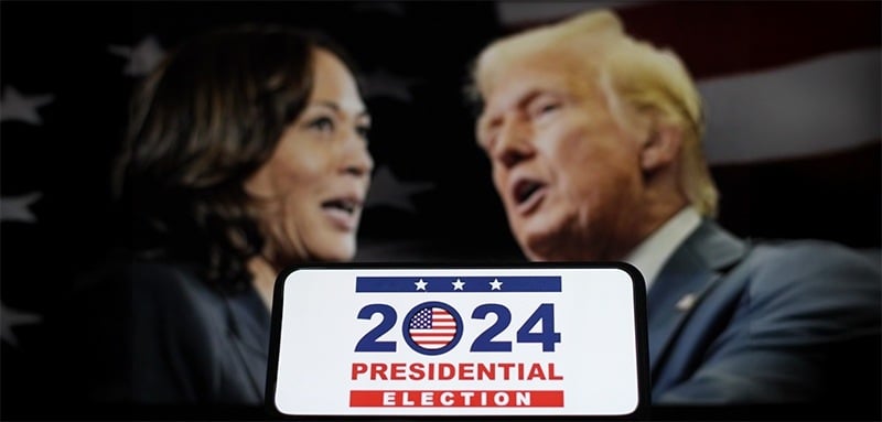 Split image: Kamala Harris on left, Donald Trump on right... both speaking. Foreground shows smartphone displaying '2024 Presidential Election' with US flag icon. American flag visible in background.